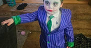 Kamrynn is registered to the contest to win money with this photo: child, face_paint, joker_costume, purple_suit, green_tie, indoor, messy_hair, carpet, toy, bucket, broom, bag, milk_crate, child_costume, black_shoes, clutter, person, portrait, costume, young_child