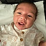 Rowan is registered to the contest to win money with this photo: baby, child, crib, cute, expression, face, happy, head, indoors, infant, light_clothing, lying_down, newborn, patterned_shirt, person, pillow, skin, smiling, tongue_out, wooden_buttons