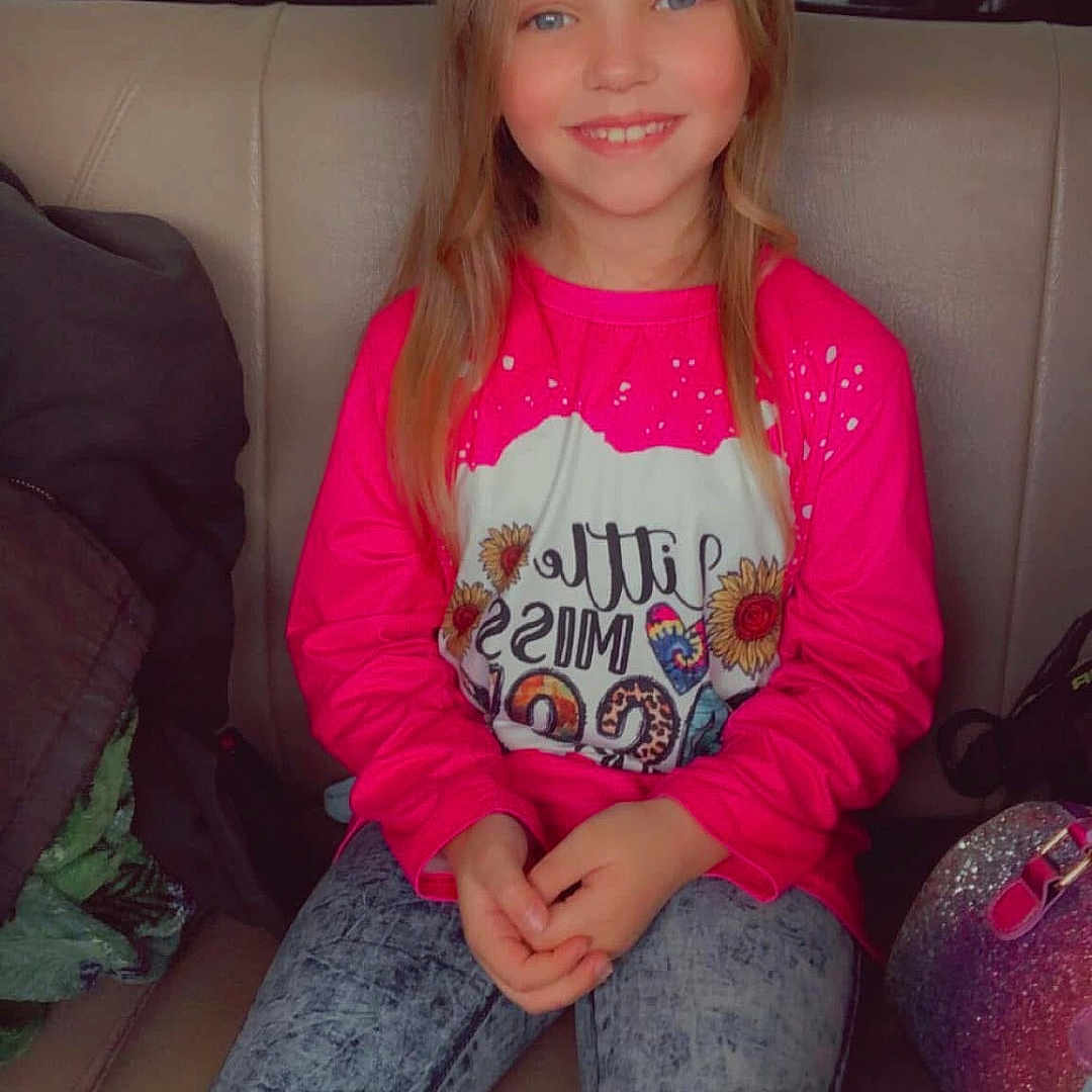 Remington joined the competition — help win amazing prizes! background, bag, blue_eyes, casual, child, clothing, girl, hands, happy, indoor, jacket, jeans, long_hair, pink_shirt, portrait, seat, sitting, smile, sunflower, window