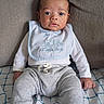 Destin is registered to the contest to win money with this photo: baby, infant, child, face, eyes, bib, clothing, pants, sitting, couch, blanket, indoor, portrait, cute, young, person, expression, textile, fabric, relaxing