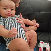 Destin joined the competition — help win amazing prizes! baby, striped_onesie, person, lap, black_couch, medicine_boxes, indoor, curious, serious, hand, skin, sitting, furniture, closeup, casual_clothing, support, home, relaxed, child, infant