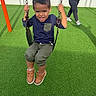 Donte is registered to the contest to win money with this photo: child, boy, swing, playground, grass, outdoor, daylight, fun, smiling, casual_clothing, shoes, adult, walking, chain, fence, recreation, activity, happy, person, leisure