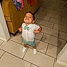 child, toddler, boy, smiling, white_shirt, bow_tie, shorts, white_shoes, standing, tiled_floor, couch, clothing, indoor, home, confident, pose, happy, furniture, casual, portrait