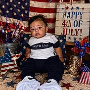 Noah is registered to the contest to win money with this photo: toddler, child, baby, american_flag, patriotic, 4th_of_july, independence_day, carpet, star_pattern, pinwheel, decorations, sign, sneakers, clothing, face, indoor, celebration, jar, lights, chair