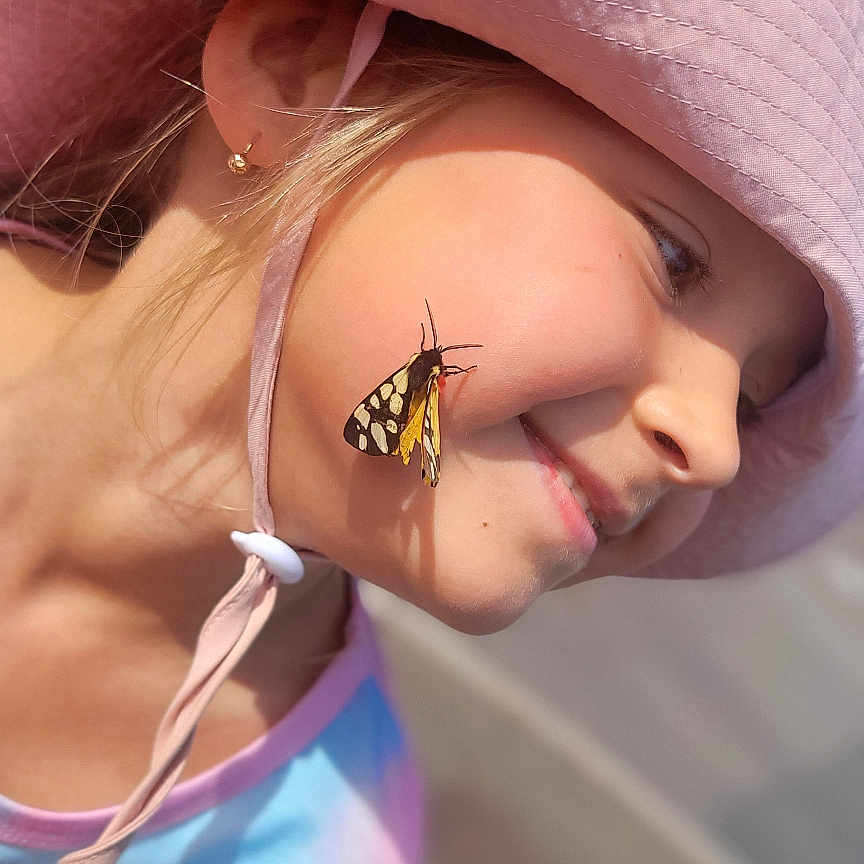 Zlata participe au concours pour gagner de l'argent avec cette photo : butterfly, casual_clothing, cheek, child, closeup, colorful, daytime, earring, face, fun, girl, happy, hat_strap, nature, outdoor, pink_hat, portrait, smile, summer, sunlight