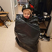 Anna participe au concours pour gagner de l'argent avec cette photo : baby, chair, child, clothing, coat, door, expression, floor, flooring, hallway, headwear, helmet, indoor, person, playful, room, shoes, smile, toddler, trash_bag