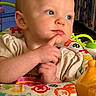baby, child, infant, face, blue_eyes, hand, finger, toy, colorful, play_area, animal_prints, clothing, indoor, expression, cute, portrait, closeup, thinking, seat, person