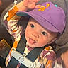 toddler, child, car_seat, purple_cap, giraffe_embroidery, hand, playful, tongue_out, straps, seatbelt, patterned_clothing, smiling, indoor, cute, baby, person, closeup, happy, seat, casual