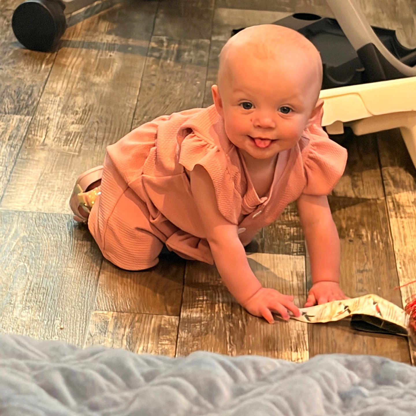 Zoey is registered to the contest to win money with this photo: baby, child, crawling, tongue_out, peach_outfit, wooden_floor, indoor, blanket, flooring, person, cute, playful, baby_clothes, head, hand, footwear, expression, home_interior, furniture, floor