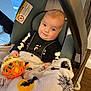 baby, infant, car_seat, blanket, toy, halloween, skeleton_outfit, smile, indoor, child, person, face, clothing, head, seatbelt, wood_floor, curious, cute, cozy, playful