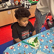 Taylin is registered to the contest to win money with this photo: child, curly_hair, black_tshirt, table, tablecloth, snowman_pattern, paper_plate, green_treat, plastic_knife, classroom, holiday_decorations, floor_tiles, person, chair, cabinet, pencil_holder, cup, wrapping_paper, food, indoor
