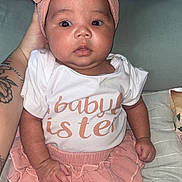Kimberley is registered to the contest to win money with this photo: arm, baby, bow, child, clothing, couch, cute, expression, hand, headband, indoors, infant, person, pillow, portrait, shirt, sitting, skirt, tattoo, young