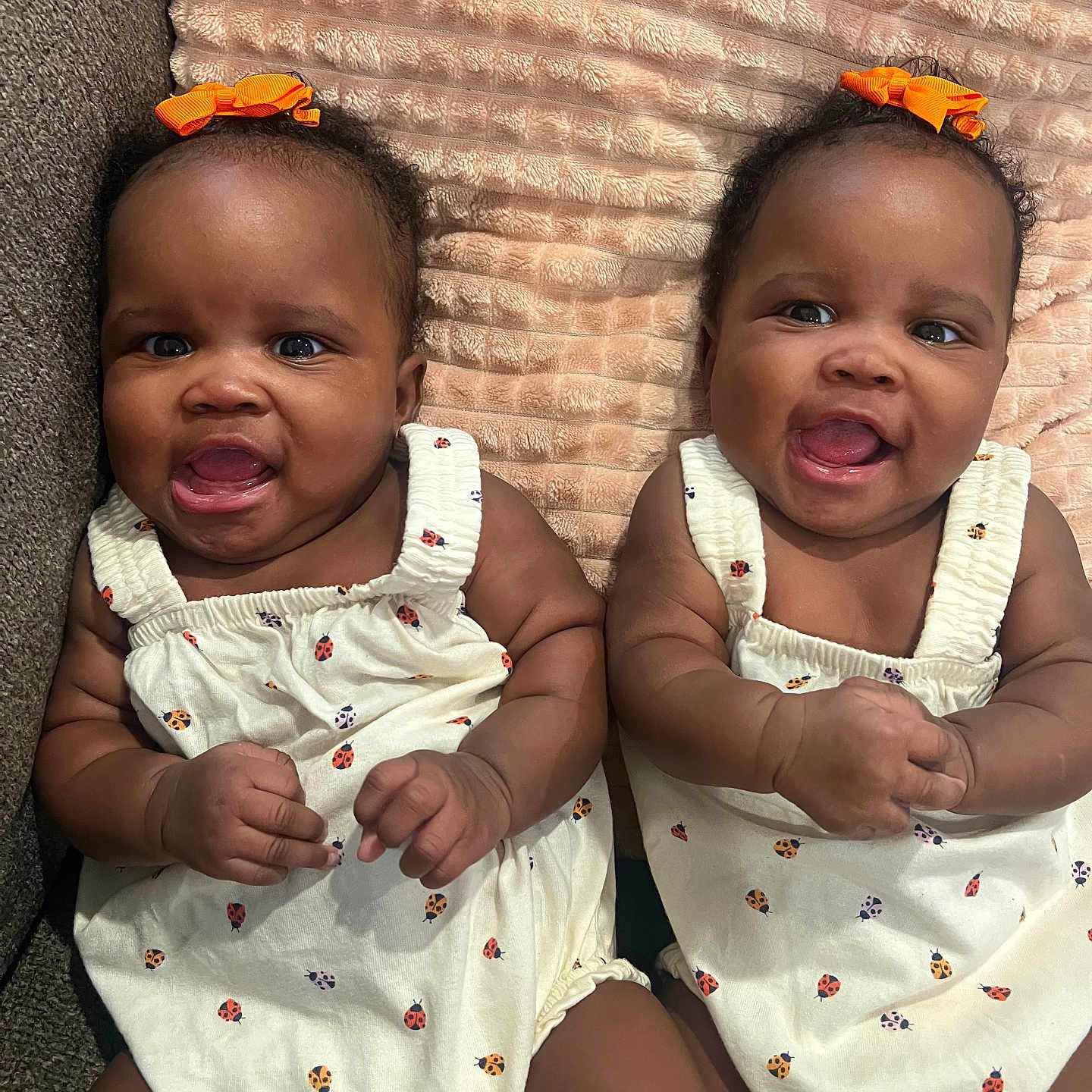 Denver And Desirae joined the competition — help win amazing prizes! baby, blanket, child, couch, cute, cute_expression, face, hands, happy, indoor, infant, ladybug_print, orange_bow, portrait, sitting, skin, smiling, toddler, twins, white_outfit