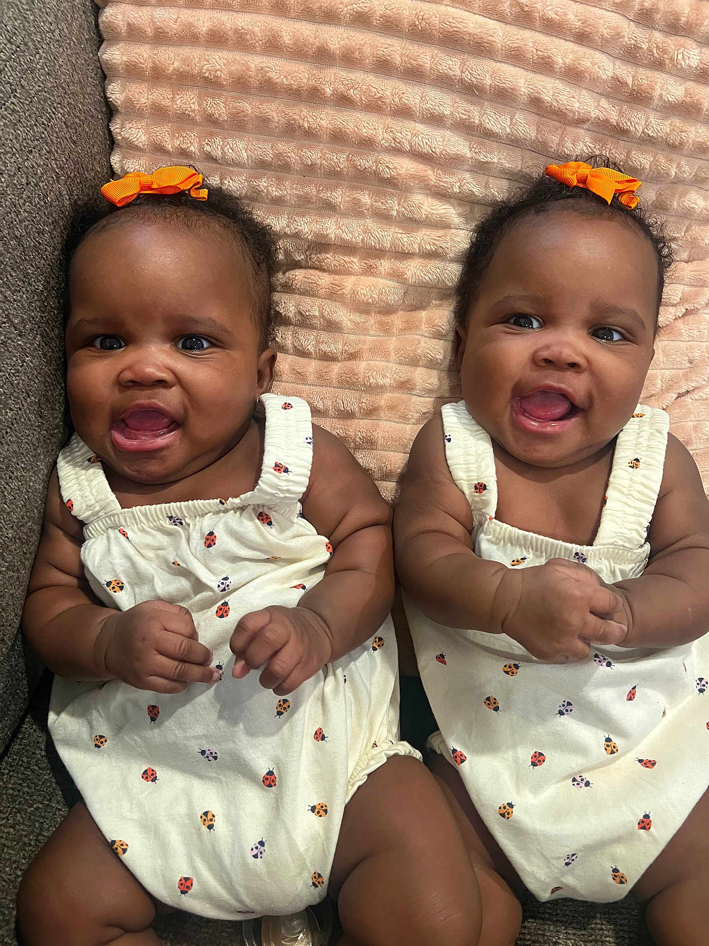 Denver And Desirae joined the competition — help win amazing prizes! baby, twins, infant, smiling, cute, orange_bow, white_outfit, ladybug_print, blanket, couch, indoor, portrait, child, happy, sitting, cute_expression, toddler, skin, face, hands