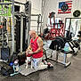 Uriah Benjamin joined the competition — help win amazing prizes! man, dog, gym, weights, exercise_equipment, red_tank_top, tattoo, kneeling, floor_mat, water_bottle, bench, barbell, fitness, muscle, indoor, sport, pet, harness, strength_training, american_flag