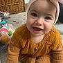 baby, infant, smiling, headband, bow, knitted_sweater, mustard_color, onesie, sitting, carpet, toys, wicker_basket, playroom, adorable, portrait, hand, eyes, cheeks, candid, indoor