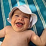 baby, infant, smiling, sun_hat, white_hat, bare_torso, laughing, tongue_out, chubby_cheeks, arm, striped_cushion, blue_background, outdoor, sunlight, joyful, close_up, portrait, skin, playful, summer