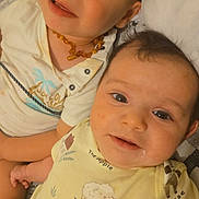 Adnan participe au concours pour gagner de l'argent avec cette photo : baby, toddler, siblings, smiling, portrait, close_up, bed, pillow, onesie, amber_necklace, infant, cute, laying_down, family, eyelashes, button_shirt, patterned_onesie, face, eyes, happy