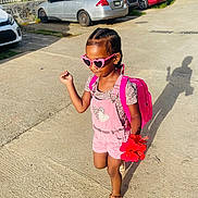 Hannah is registered to the contest to win money with this photo: child, girl, pink_sunglasses, backpack, flower, sidewalk, sunlight, shadow, car, parking_lot, summer_clothing, shorts, sandals, braided_hair, outdoor, happy, walking, casual, playful, bright_colors