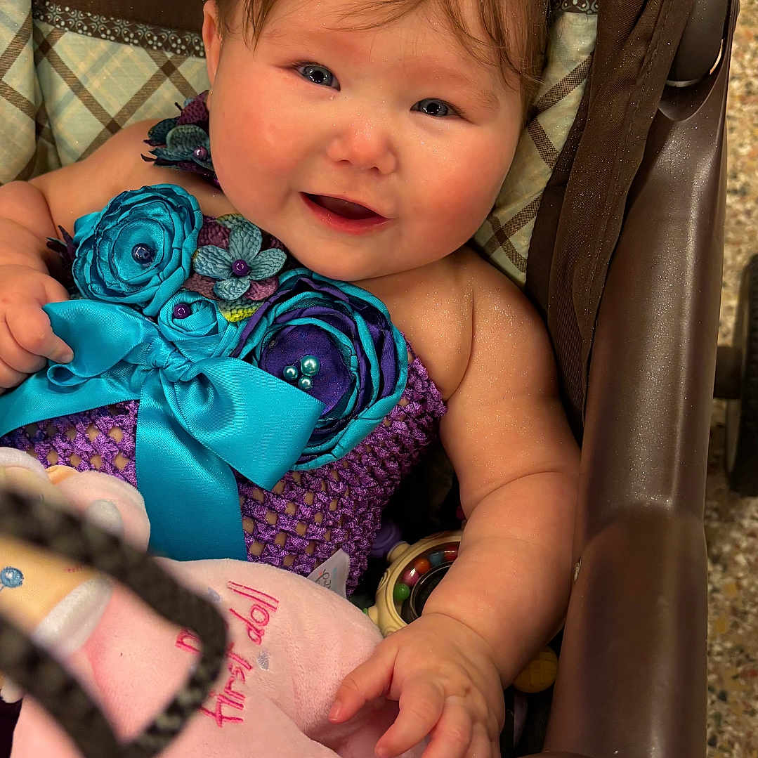 Lorelie joined the competition — help win amazing prizes! baby, child, stroller, purple_outfit, blue_flowers, bow, plush_toy, brush, pacifier, happy, smiling, cute, rosy_cheeks, indoor, person, infant, seated, toy, hand, face