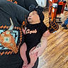 baby, newborn, infant, gloves, foam_fingers, headband, black_clothing, adult_arm, tattoo, graphic_tshirt, store, hair_extensions, wood_floor, person, holding, sleeping, cute, indoor, shopping, apparel