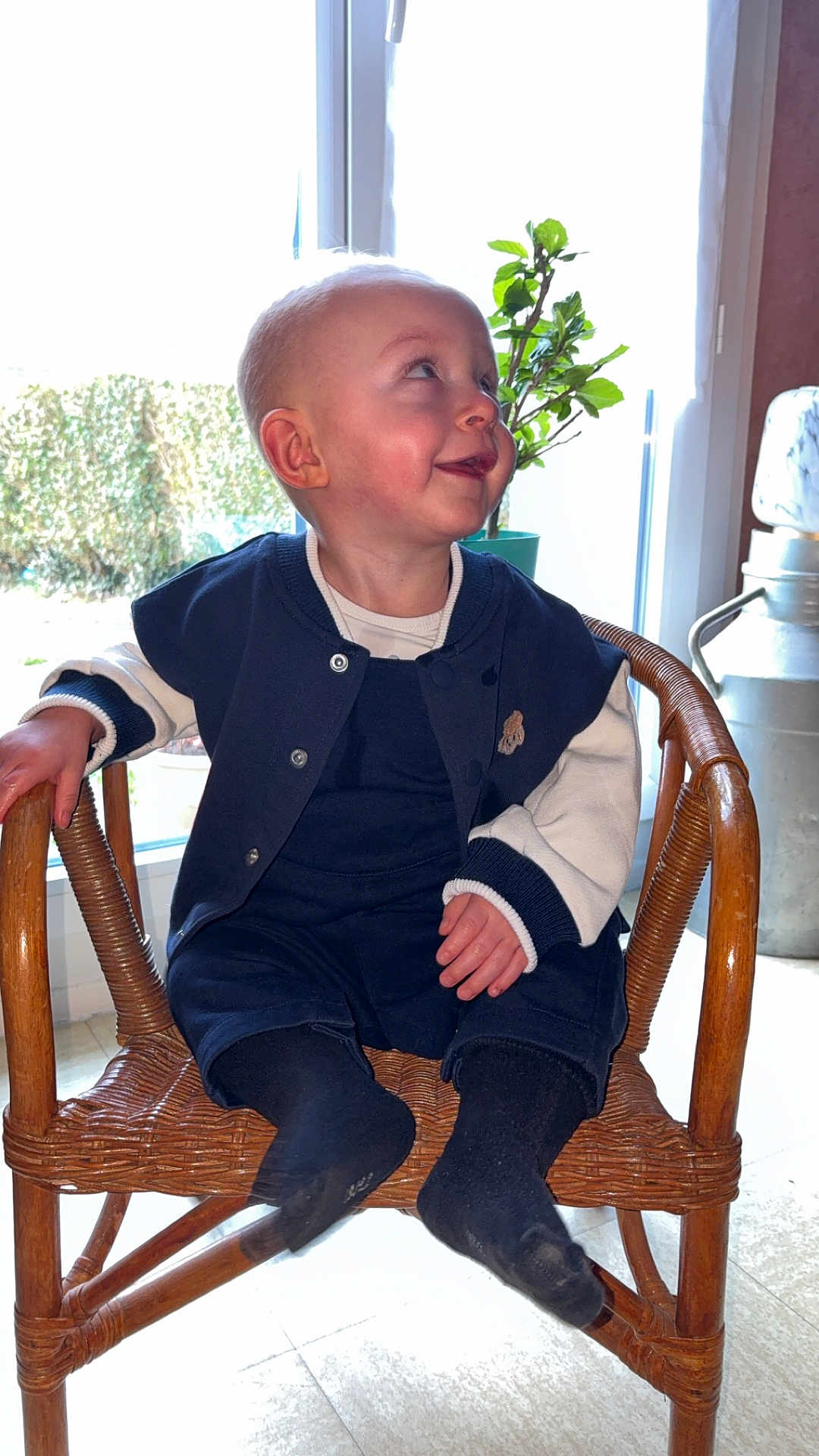 Ewen a rejoint le concours — aidez-le/la à gagner de superbes lots ! baby, child, smiling, sitting, chair, wicker_chair, indoor, window, plant, green_plant, clothing, black_socks, happy, face, head, person, floor, light, cozy, casual