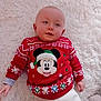 Ewen a rejoint le concours — aidez-le/la à gagner de superbes lots ! baby, infant, child, mickey_mouse, christmas_sweater, red_sweater, white_pants, lying_down, blanket, soft_texture, holiday_theme, cute, smiling, face, head, hand, cozy, indoors, portrait, festive