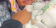 Milani is registered to the contest to win money with this photo: baby, smiling, curly_hair, blanket, car_seat, pink, black, hand, person, infant, happy, cozy, child, seatbelt, clothing, portrait, indoors, cute, comfort, toddler