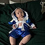 baby, child, infant, blue_clothing, boxing_gloves, boxing_outfit, blanket, green_blanket, bed, pillow, indoor, person, cute, sitting, portrait, looking_at_camera, soft_lighting, skin, small_person, relaxed