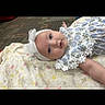 Hadley is registered to the contest to win money with this photo: baby, infant, blanket, headband, blue_eyes, floral_dress, carpet, floor, person, child, cute, indoors, portrait, laying_down, soft_texture, white, pink, yellow, patterned, young
