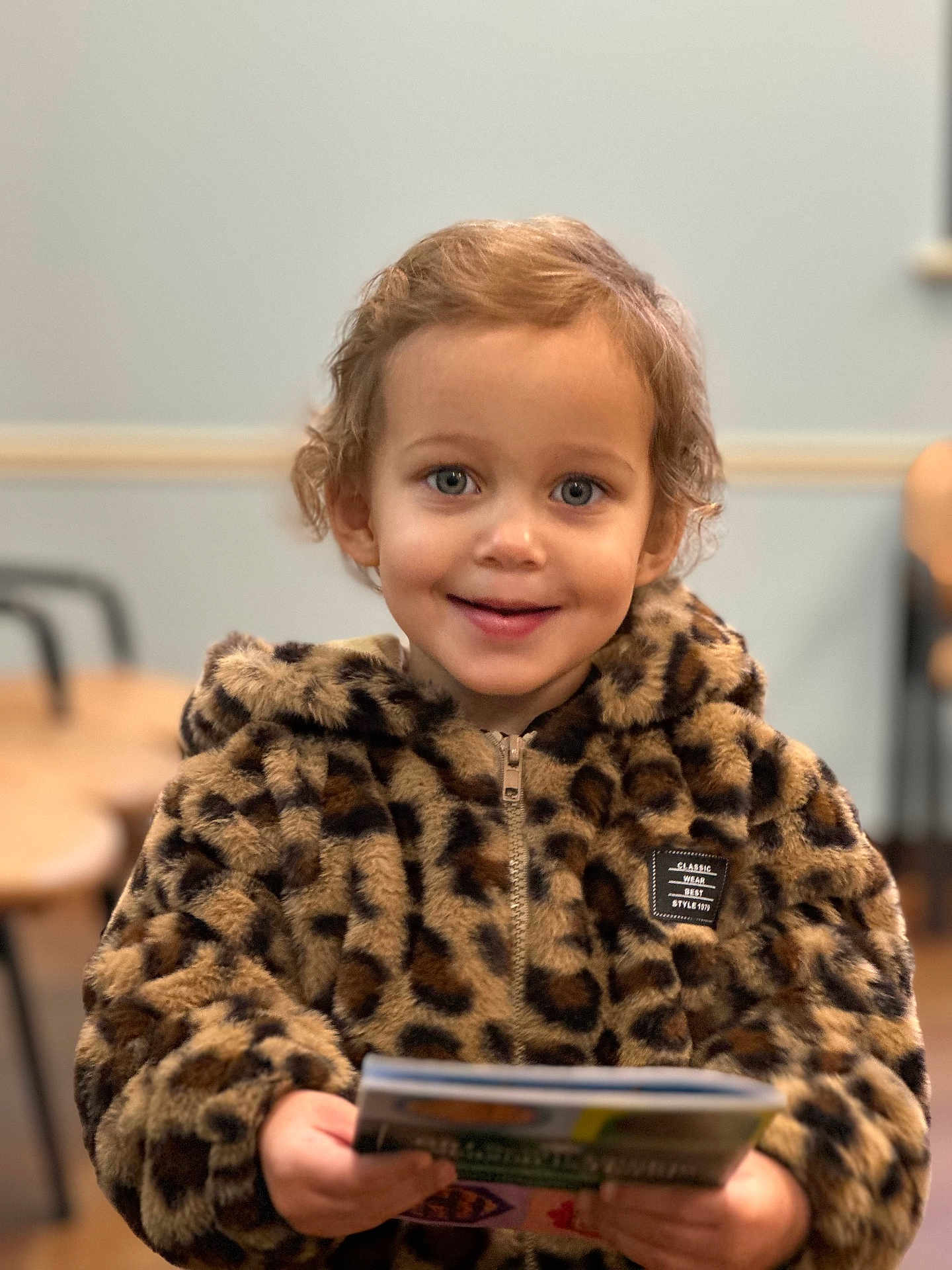 Bella is registered to the contest to win money with this photo: baby, bodypart, clothing, coat, face, finger, hand, happy, head, jacket, knitwear, longsleeve, person, photography, portrait, reading, sleeve, smile, sweater, text
