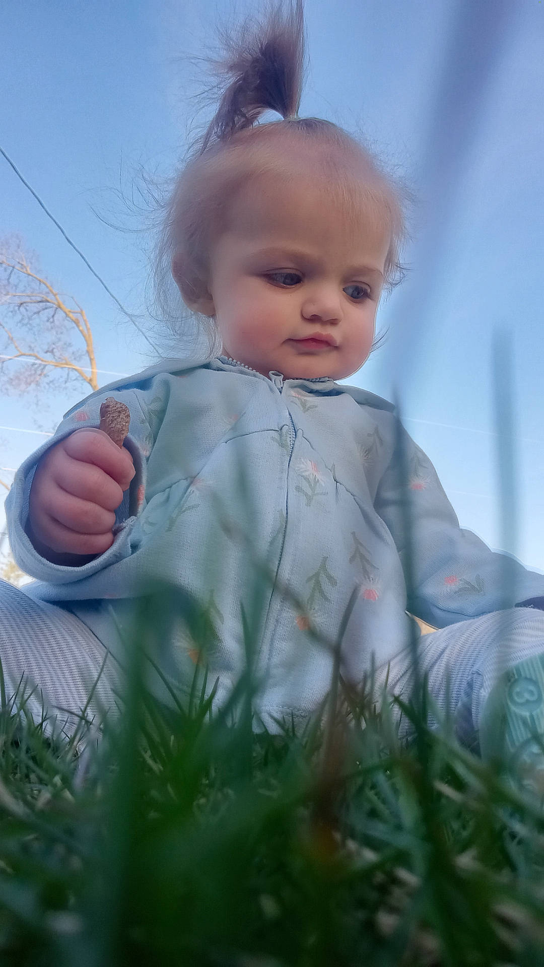 Skye is registered to the contest to win money with this photo: baby, bodypart, clothing, coat, face, finger, grass, hand, happy, head, jacket, knitwear, longsleeve, person, photography, plant, portrait, sleeve, smile, sweater