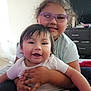 Avery Mae Zuniga joined the competition — help win amazing prizes! baby, blanket, child, clothing, couch, curtain, face, furniture, glasses, hair, happy, hugging, indoor, person, room, sitting, skin, smiling, television, window
