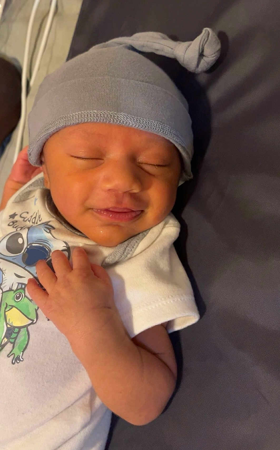 Lucario is registered to the contest to win money with this photo: baby, infant, hat, onesie, sleeping, smile, hand, cute, child, face, peaceful, clothing, resting, portrait, babywear, knotted_hat, animal_print, indoors, skin, newborn