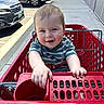 Mickey is registered to the contest to win money with this photo: baby, child, shopping_cart, red, blue_eyes, striped_shirt, outdoor, sidewalk, parking_lot, car, smiling, happy, person, toddler, hand, daylight, concrete, metal, urban, casual_clothing