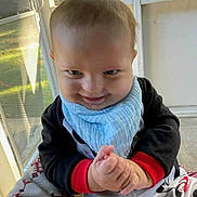 Lamarri is registered to the contest to win money with this photo: baby, child, indoor, window, sunlight, pajamas, blue_bib, hands, clothing, face, smile, expression, person, young_child, fingers, seat, background, room, light, casual