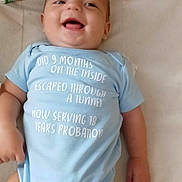 Lamarri is registered to the contest to win money with this photo: baby, baby_wipes, bed, blue_clothing, child, cute, face, hand, happy, humor, indoors, infant, leg, lying_down, onesie, portrait, skin, smiling, soft_surface, text_on_clothing