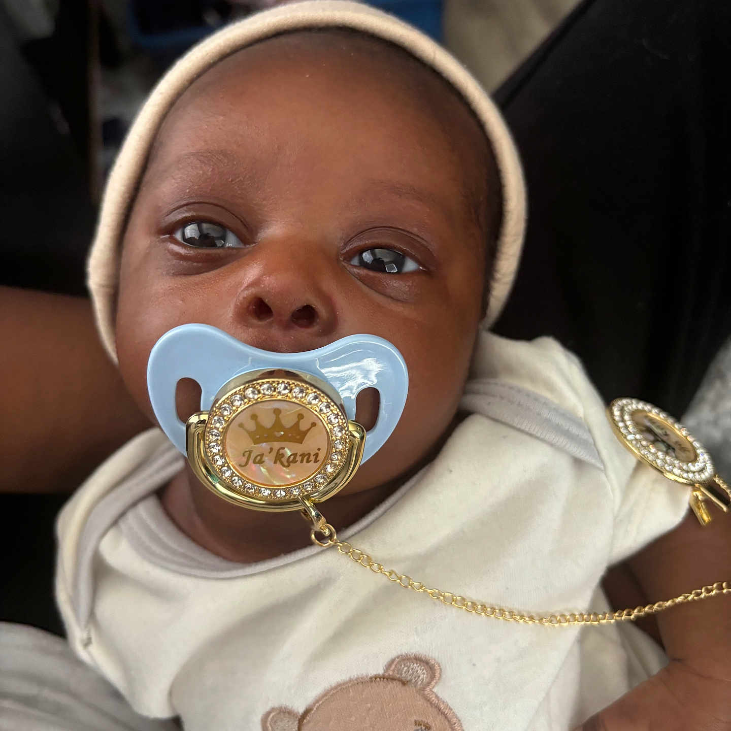 Jakani joined the competition — help win amazing prizes! baby, infant, pacifier, hat, clothing, cute, face, hand, teddy_bear, embroidery, indoor, person, newborn, child, closeup, adorable, lying_down, soft_lighting, skin, expression