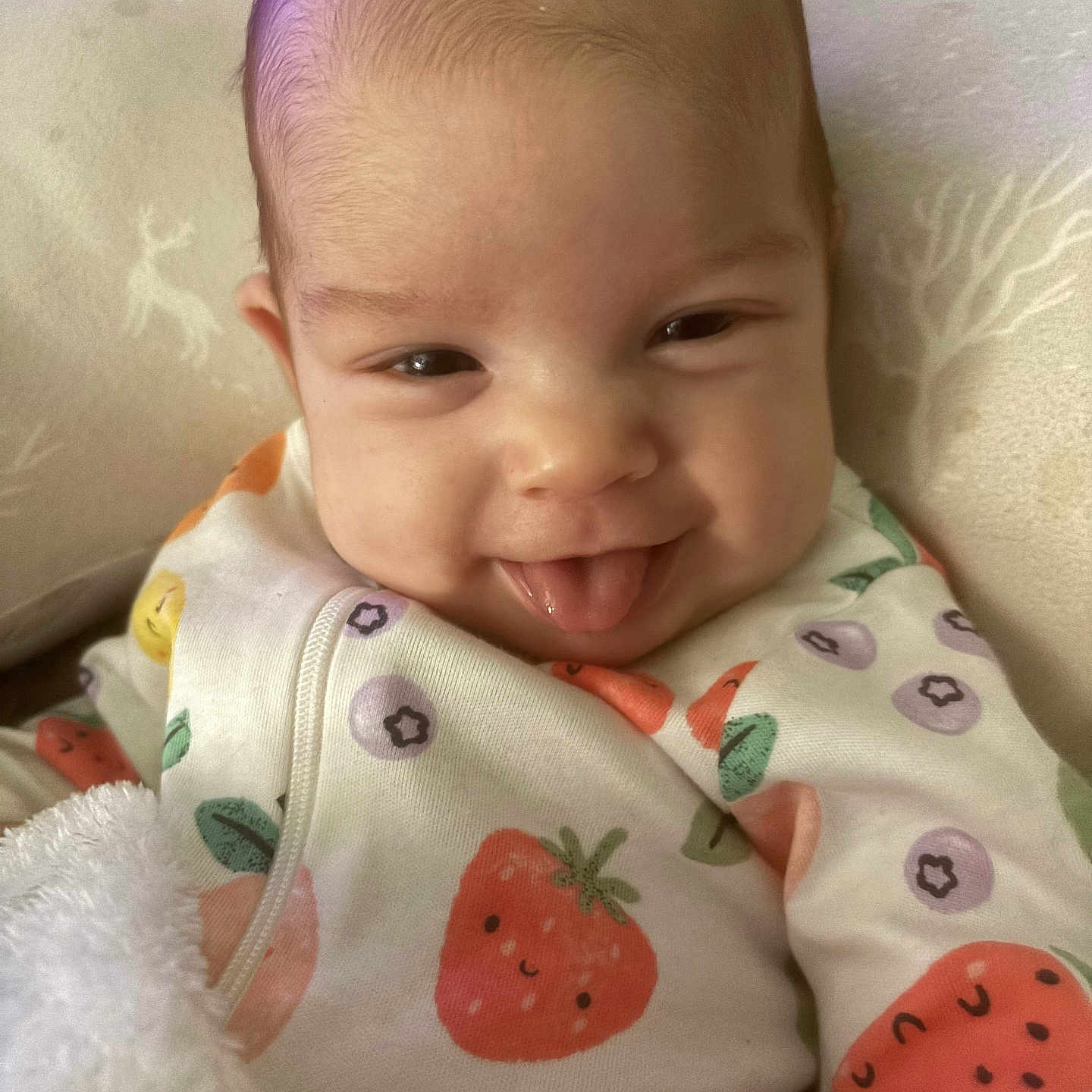 Alynn is registered to the contest to win money with this photo: baby, blanket, child, closeup, cozy, cushion, cute, expression, face, fruit_pattern, happy, head, indoor, infant, onesie, person, portrait, smiling, soft, tongue_out