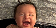 Kaia is registered to the contest to win money with this photo: baby, smiling, infant, cute, pigtails, happy, child, face, pink_dress, patterned_blanket, bow, lying_down, indoors, portrait, young_child, joyful, skin, person, baby_clothes, toddler