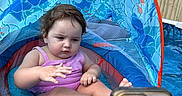 Amina is registered to the contest to win money with this photo: toddler, child, swimsuit, inflatable_pool, pool_float, canopy, smartphone, water, backyard, summer, outdoor, trees, fence, baby, sitting, concentration, play, fun, sunny, recreation