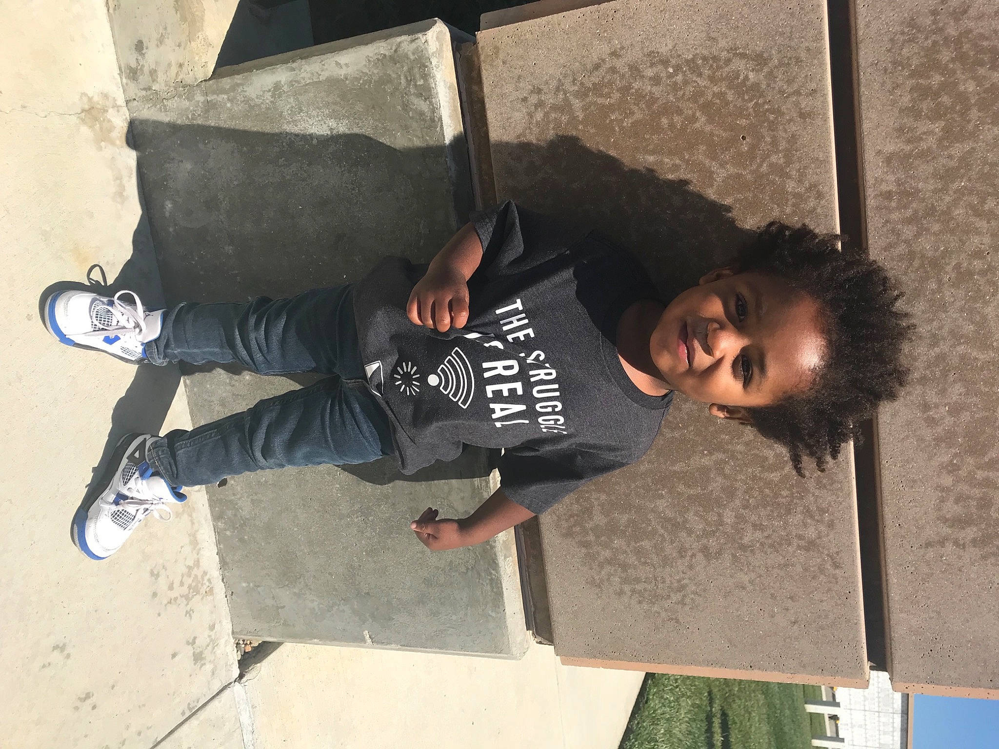 Jakai is registered to the contest to win money with this photo: child, concrete, denim, elbow, fun, happy, joy, leisure, outdoor_shoe, person, recreation, shade, shadow, shoe, smile, sneakers, street_fashion, t_shirt, walking_shoe, wall
