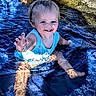 child, toddler, water, splashing, smiling, blue, tank_top, outdoor, happy, face, barefoot, legs, summer, nature, sunlight, rocks, playful, person, reaching_hand, pool