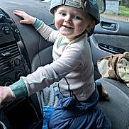 Aladar is registered to the contest to win money with this photo: child, toddler, car, backwards_cap, smile, kneeling, seat, dashboard, clothing, window, hand, bag, toy, blanket, indoor, playful, face, person, happy, casual