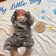Isaiah is registered to the contest to win money with this photo: baby, infant, pacifier, blanket, onesie, gray_clothing, striped_clothing, wooden_plaque, text, stars, elephant, blue_text, yellow_stars, soft_texture, lying_down, raised_arm, footwear, newborn, three_months, cute