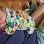 baby, newborn, sleeping, drool, onesie, floral_pattern, person, tattoo, denim_shorts, couch, hand, skin, closeup, indoor, relaxation, cozy, comfort, casual_clothing, resting, human