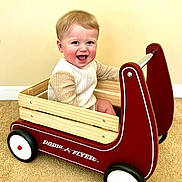 Leo joined the competition — help win amazing prizes! baby, child, smiling, wagon, radio_flyer, toy, indoor, carpet, wood, red, white, face, happy, sitting, person, clothing, sleeves, play, fun, cute