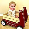 baby, child, smiling, wagon, radio_flyer, toy, indoor, carpet, wood, red, white, face, happy, sitting, person, clothing, sleeves, play, fun, cute