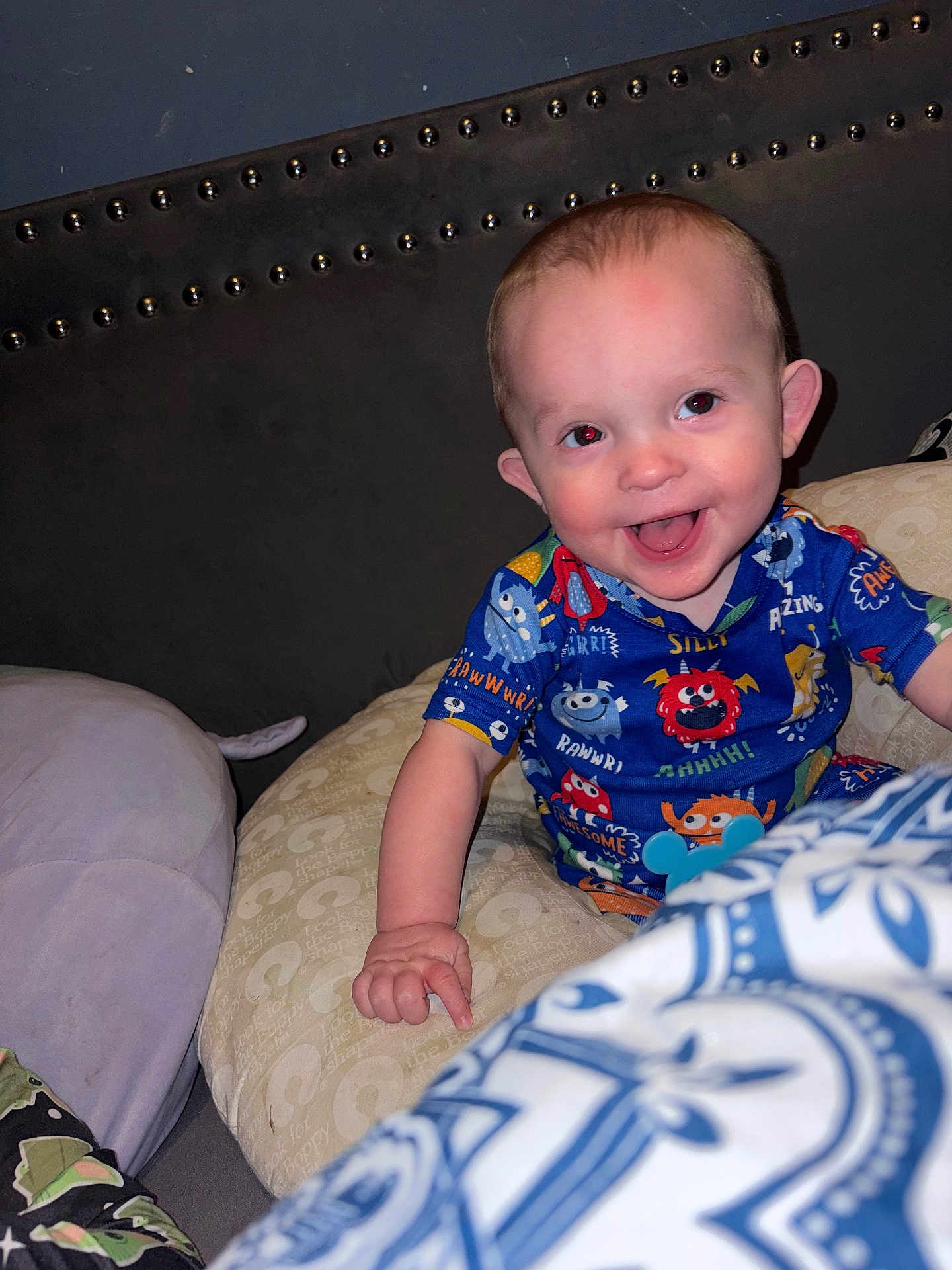 Asher is registered to the contest to win money with this photo: baby, infant, smiling, pajamas, pillow, bed, headboard, red_eye, ear, hand, blanket, indoor, flash, bedroom, happy, person, sitting, cute, nursery, patterned_clothing