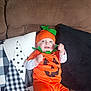 baby, infant, pumpkin_costume, halloween, couch, pillow, orange_outfit, smile, happy, costume, hat, green_leaf, jack_o_lantern, plush, sitting, indoor, portrait, eyes, fabric, cute